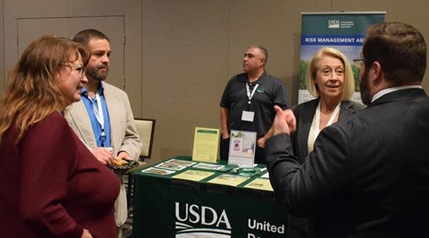 Five people standing and talking at USDA conference booth 